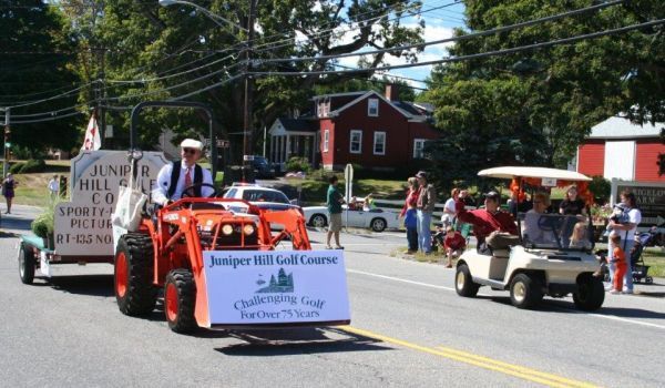 A man is driving a tractor with a sign that says juniper hill golf course