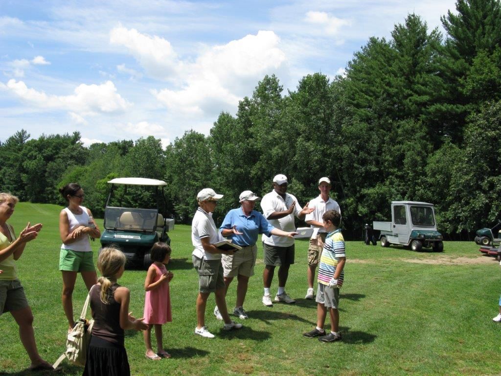 A group of people standing in a grassy field with a golf cart in the background