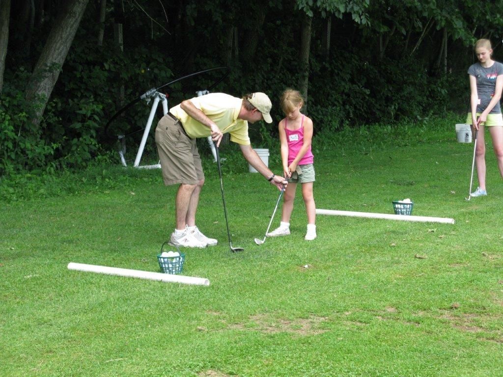 A man is teaching a little girl how to play golf