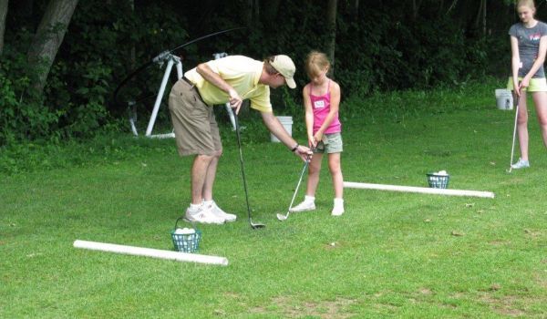 A man is teaching a little girl how to play golf