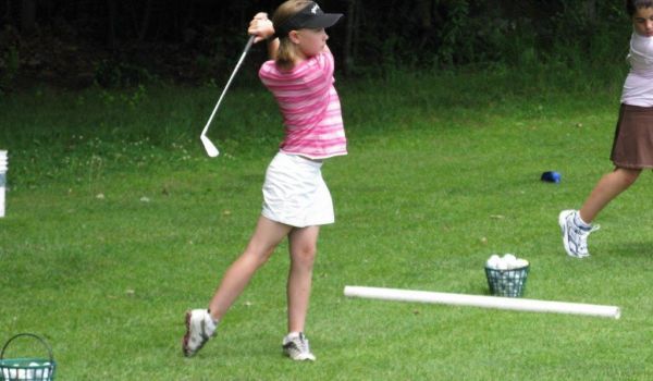 A girl is swinging a golf club on a golf course
