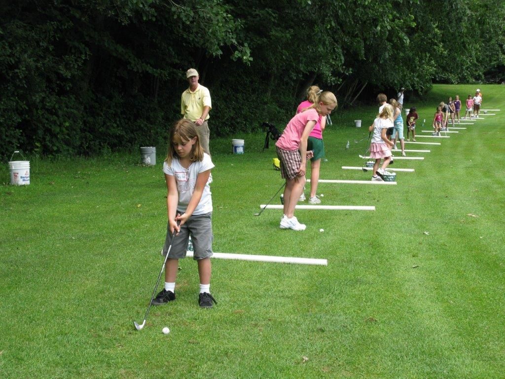 A group of children are practicing golf on a lush green field