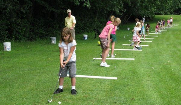 A group of children are practicing golf on a lush green field