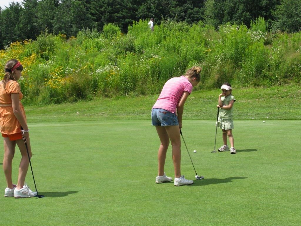 A group of young girls are playing golf on a green.
