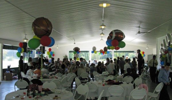 A large room with tables and chairs and balloons hanging from the ceiling.