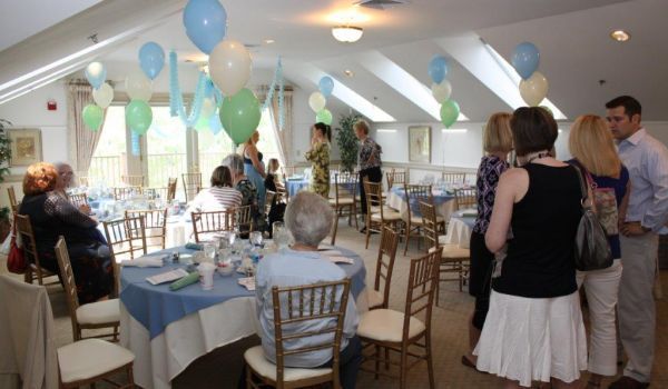 A group of people are sitting at tables in a room with balloons hanging from the ceiling.