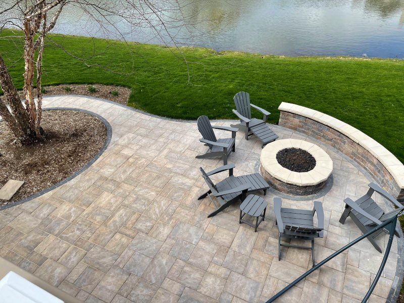 A patio with a fire pit and chairs next to a lake.