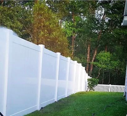 A white fence surrounds a lush green yard with trees in the background.