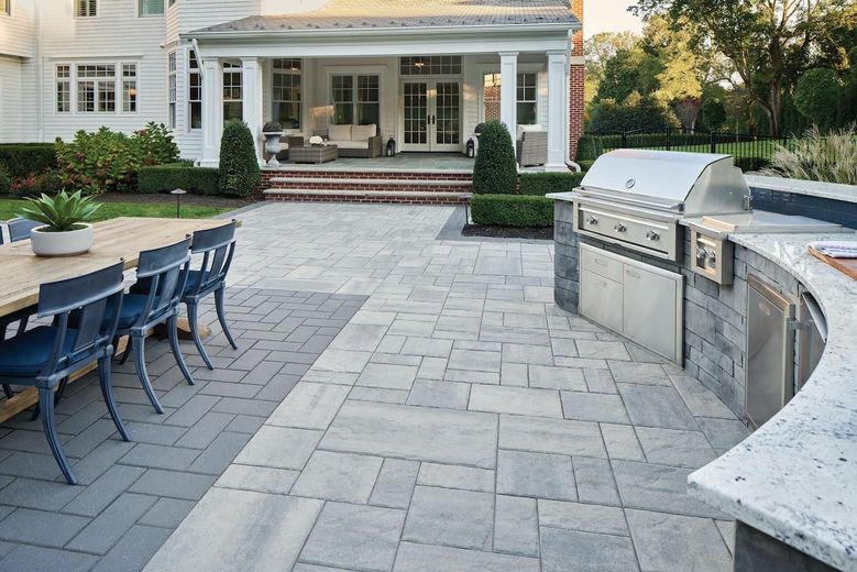 A patio with a table and chairs and a grill in front of a house.