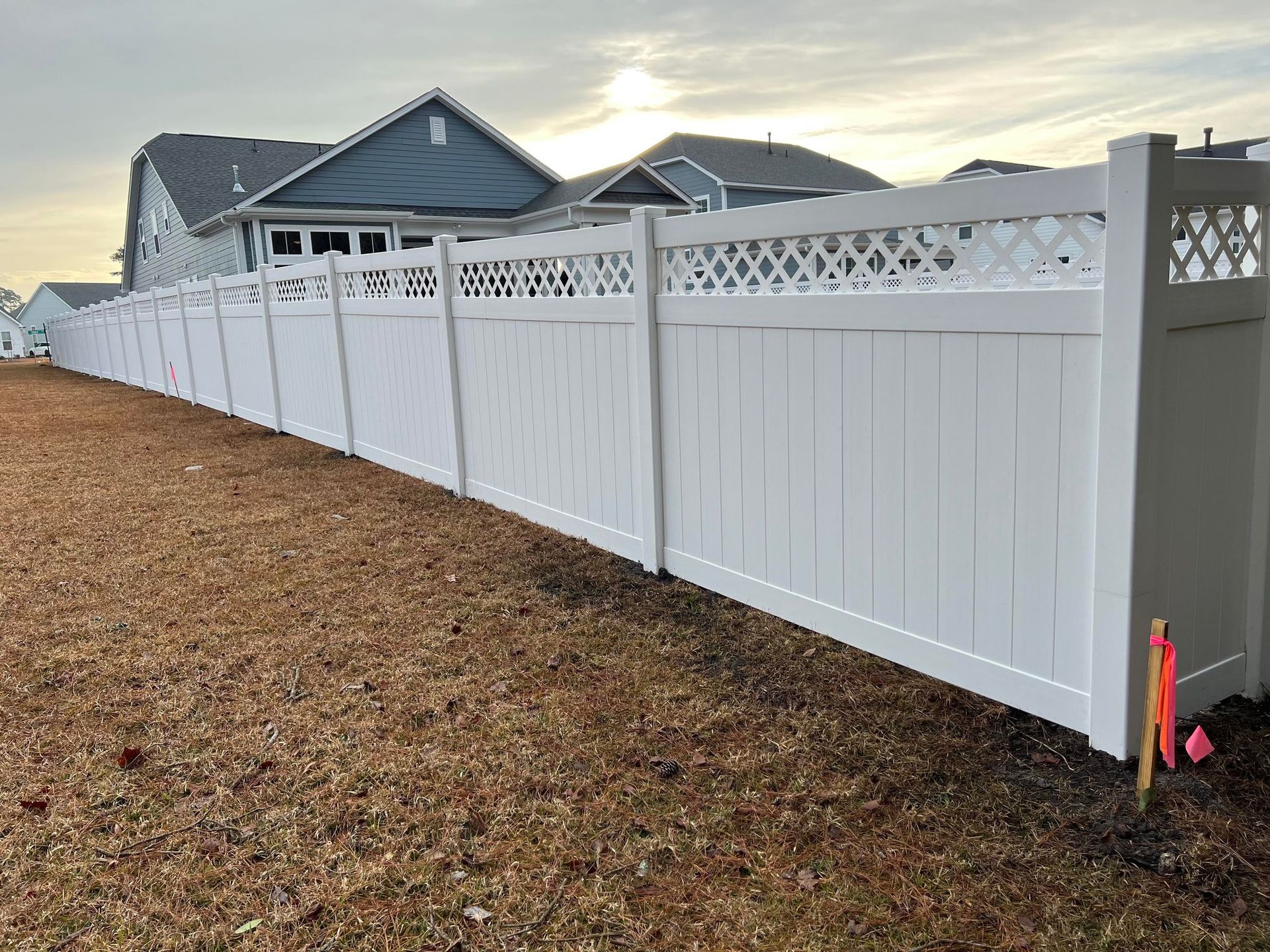 A white vinyl fence is sitting on top of a dirt field next to a house.