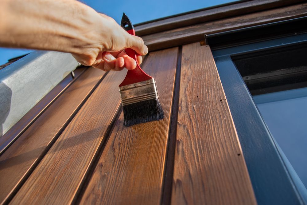 A Hand Holding a Red-handled Brush Applies Stain to Textured Wood — Strait Edge Painting In Tweed Heads, NSW