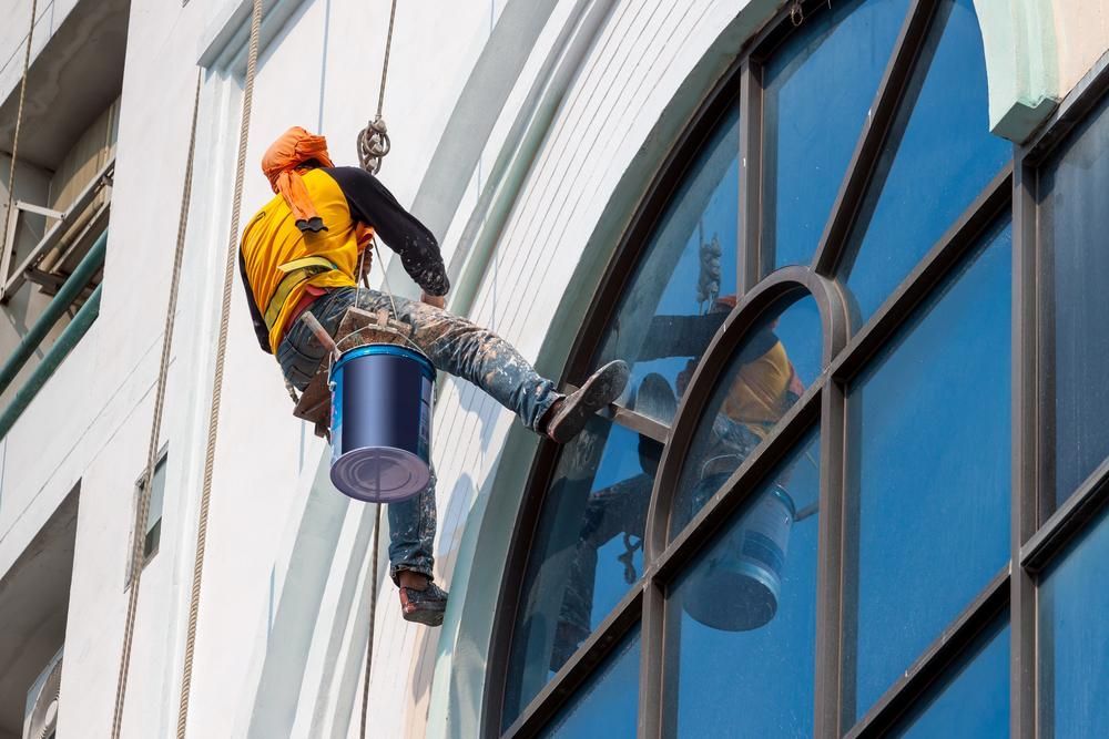 A Man Is Painting The Side Of A Building With A Bucket — Strait Edge Painting In Byron Bay, NSW