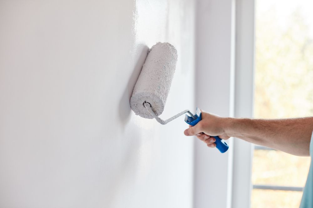 A Person Uses a Paint Roller to Apply White Paint to a Wall — Strait Edge Painting In Gold Coast, NSW