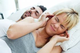 A woman is covering her ears while a man sleeps in the background.