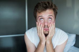 A man is sitting on a bed with his hands on his face.