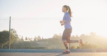 A woman is running on a sidewalk in front of a chain link fence.