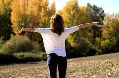 A woman is standing in a field with her arms outstretched.