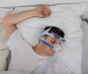 A man is sleeping in a bed with an oxygen mask on his face.