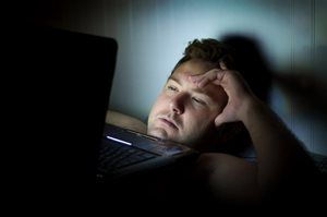 A man is laying in bed looking at a laptop computer.