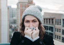 A woman wearing a hat and a coat is holding a napkin to her mouth.