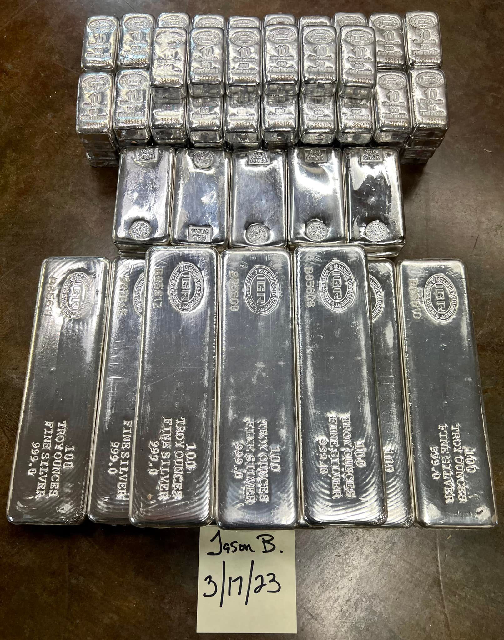 Rows of silver bars stacked on a dark table, with a small handwritten label below.