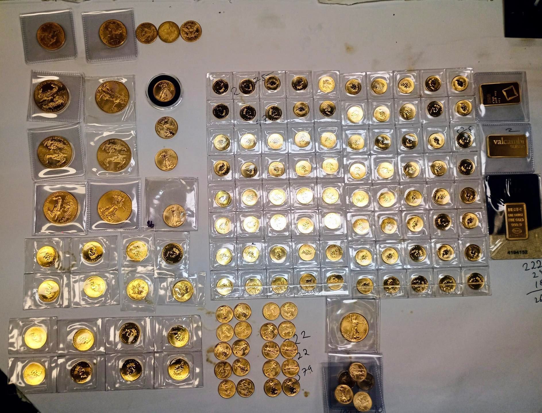 Gold coins and bars in plastic sleeves spread out on a surface, likely for display or assessment.