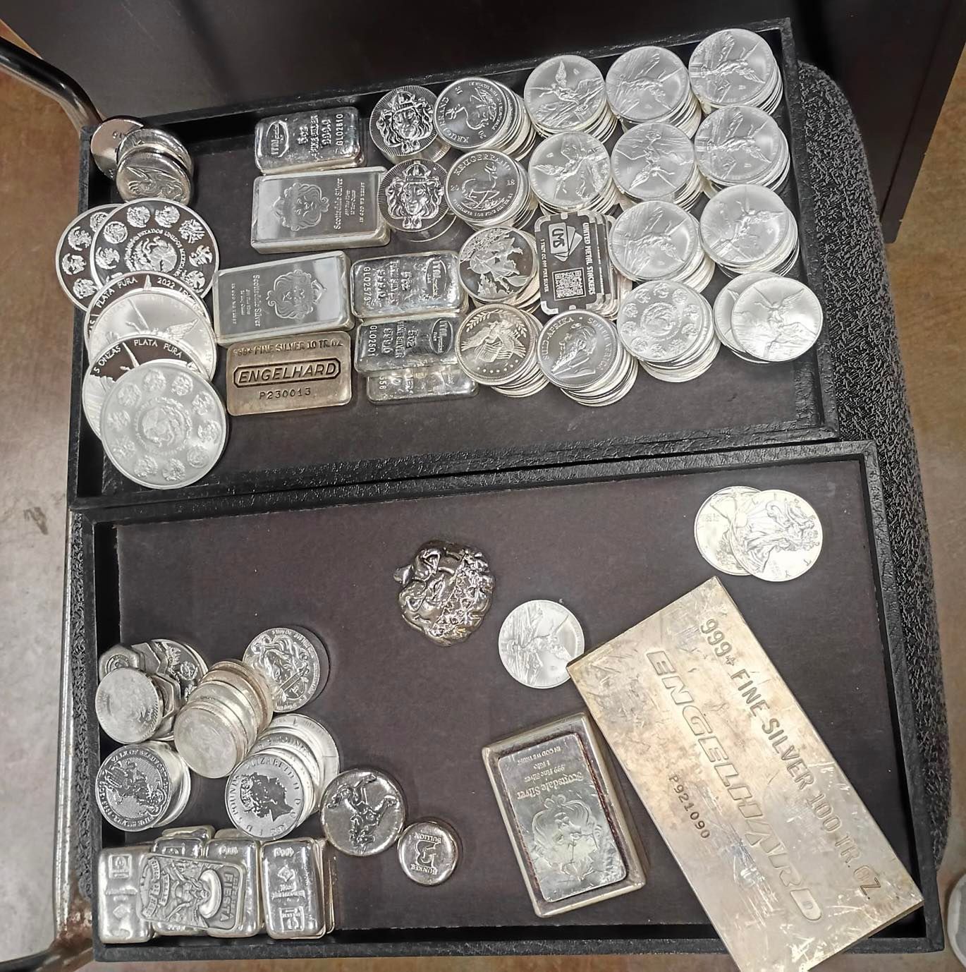 Silver coins and bars displayed in black trays.