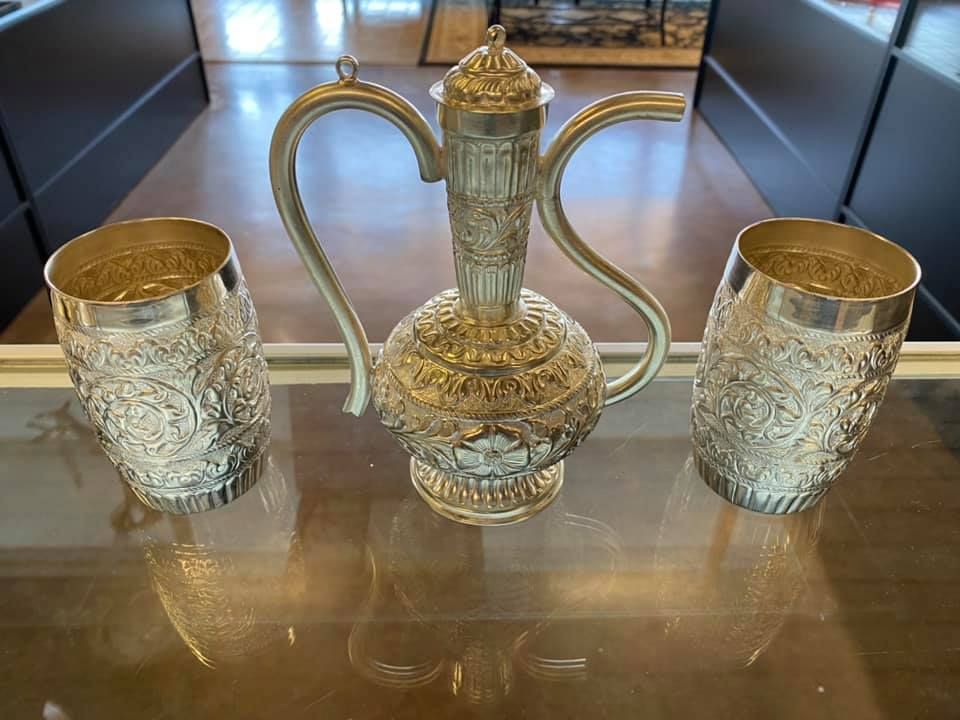A silver pitcher and two cups are sitting on a glass table.