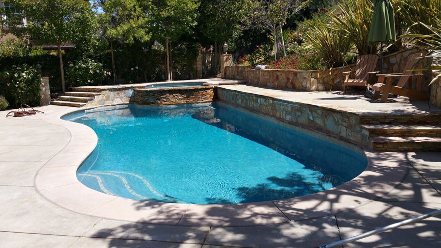 A large swimming pool surrounded by trees and stairs in a backyard.