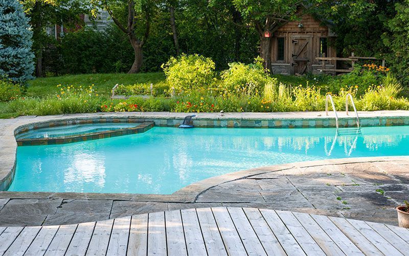A large swimming pool surrounded by trees and a wooden deck.