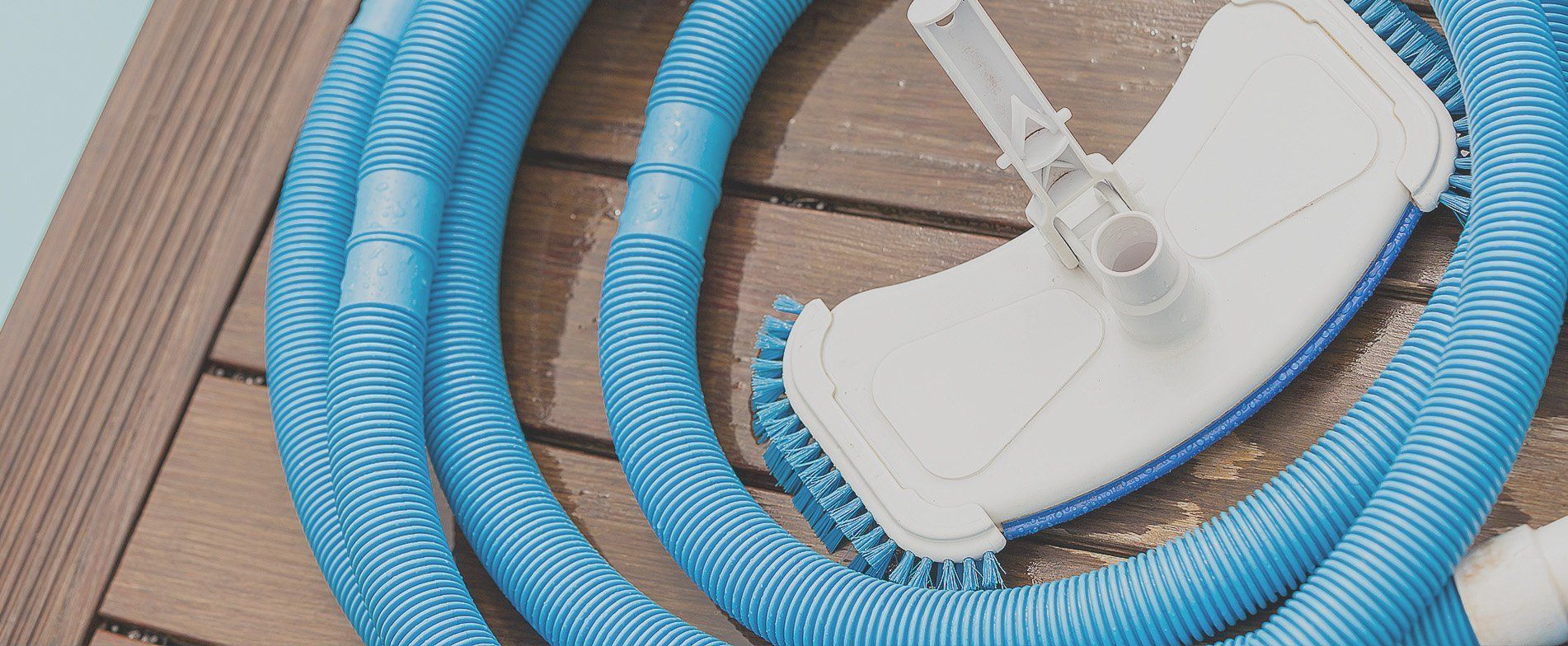 A hose and a vacuum cleaner are sitting on a wooden deck next to a swimming pool.