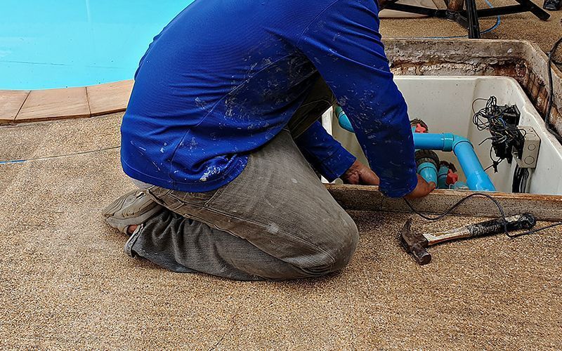 A man is kneeling on the ground working on a swimming pool.