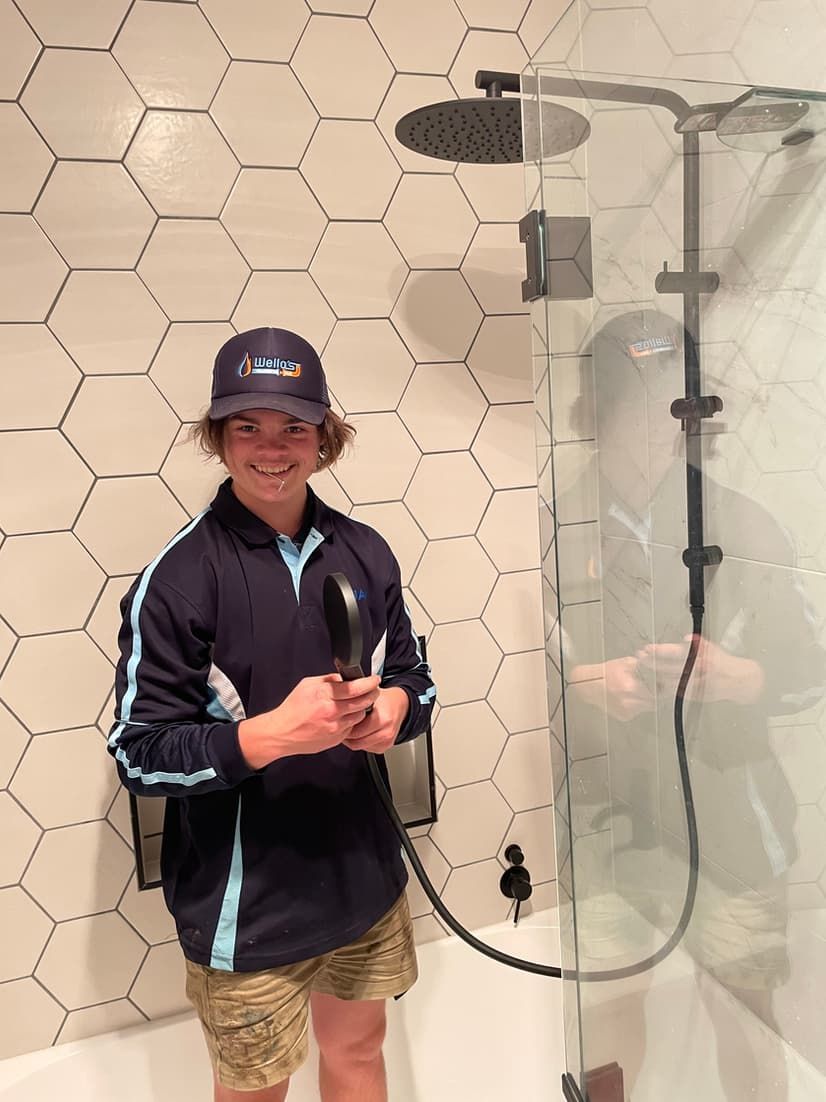 A Man is Standing in a Shower Holding a Shower Head — Wello's Plumbing & Gas In Thurgoona, NSW