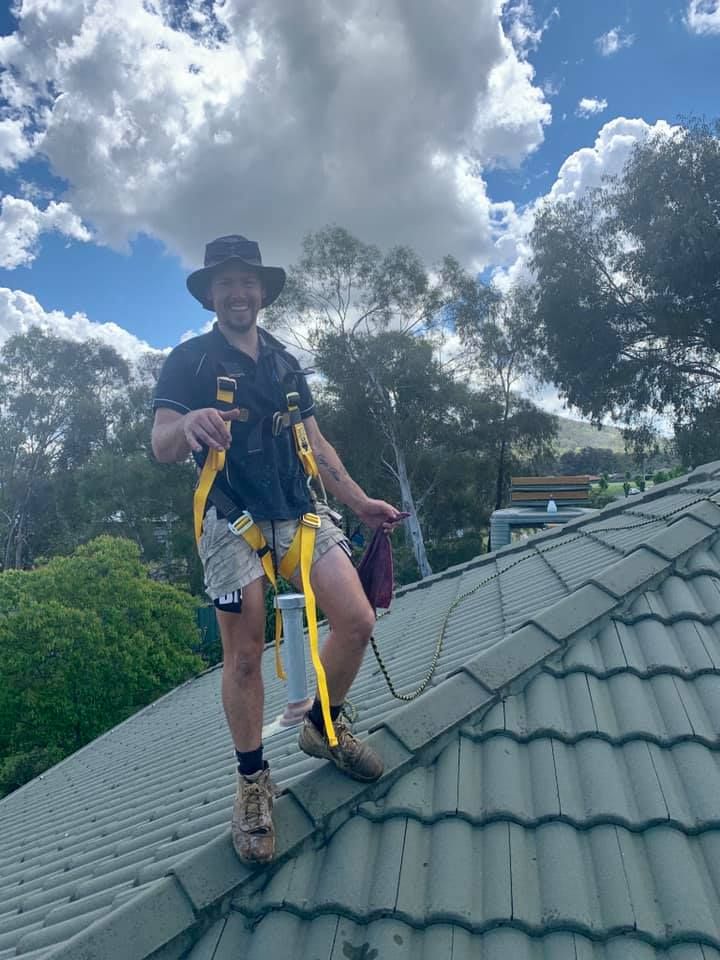 A Man Is Standing On A Roof With Safety Staps— Wello's Plumbing & Gas In Thurgoona, NSW