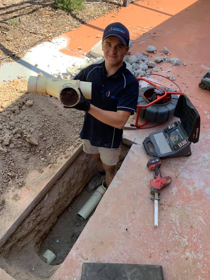 A Man Is Standing In A Hole In the Ground Holding A Pipe — Wello's Plumbing & Gas In Thurgoona, NSW
