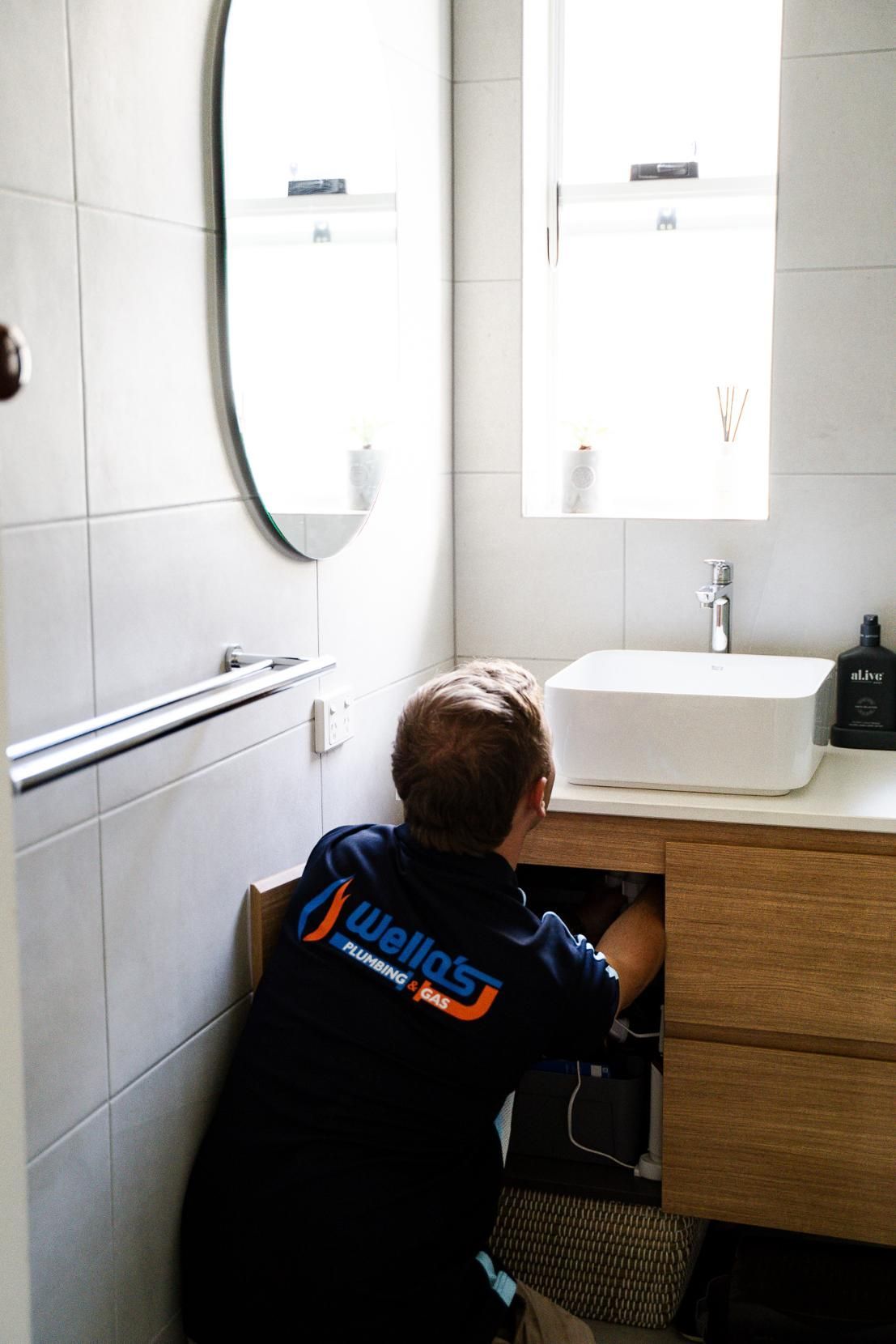 A Man is Fixing a Sink in a Bathroom — Wello's Plumbing & Gas In Lavington, NSW