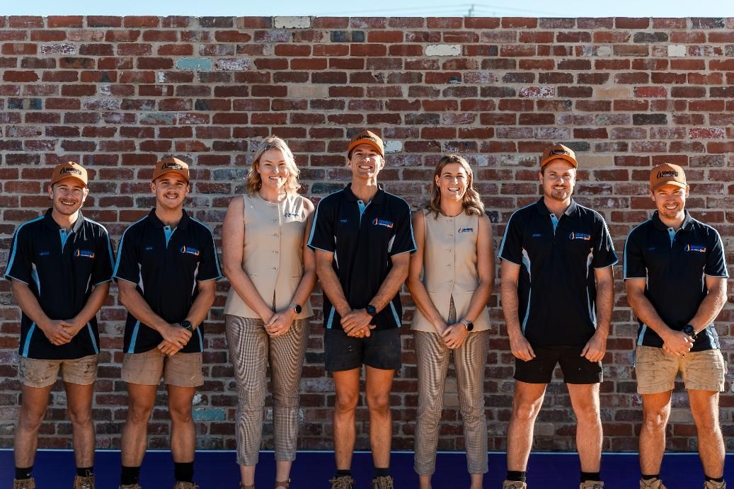 A Group of People Are Standing in Front of a Brick Wall — Wello's Plumbing & Gas In Lavington, NSW