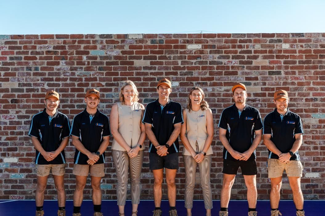 A Group of People Are Standing in Front of a Brick Wall — Wello's Plumbing & Gas In Wodonga, VIC