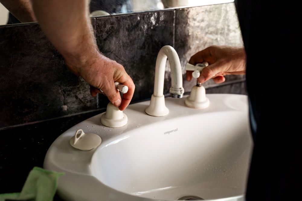 A Person Is Adjusting a Bathroom Sink Faucet — Wello's Plumbing & Gas in Thurgoona, NSW