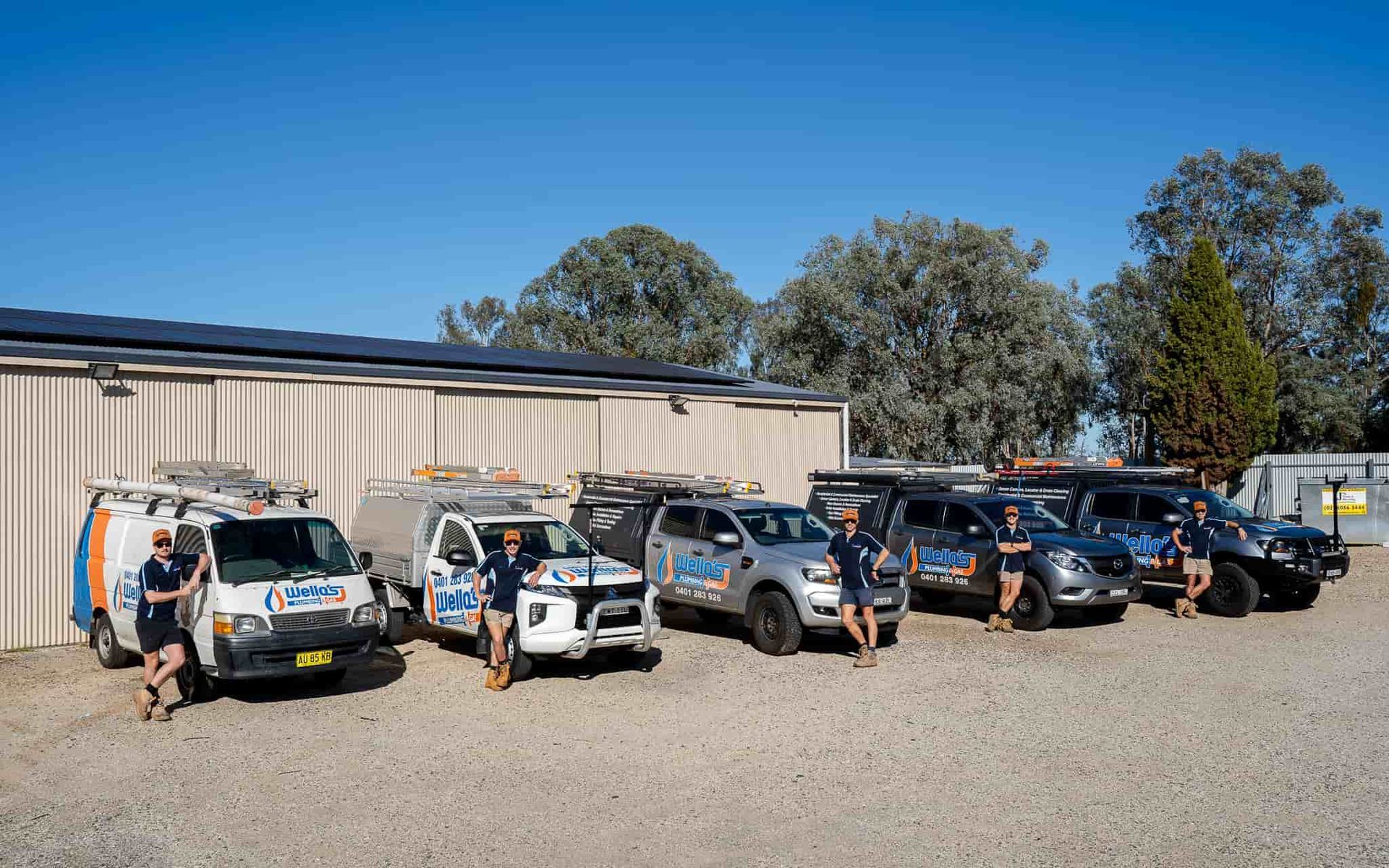 A Group of People Standing in Front of a Row of SUV's and Truck — Wello's Plumbing & Gas In Thurgoona, NSW