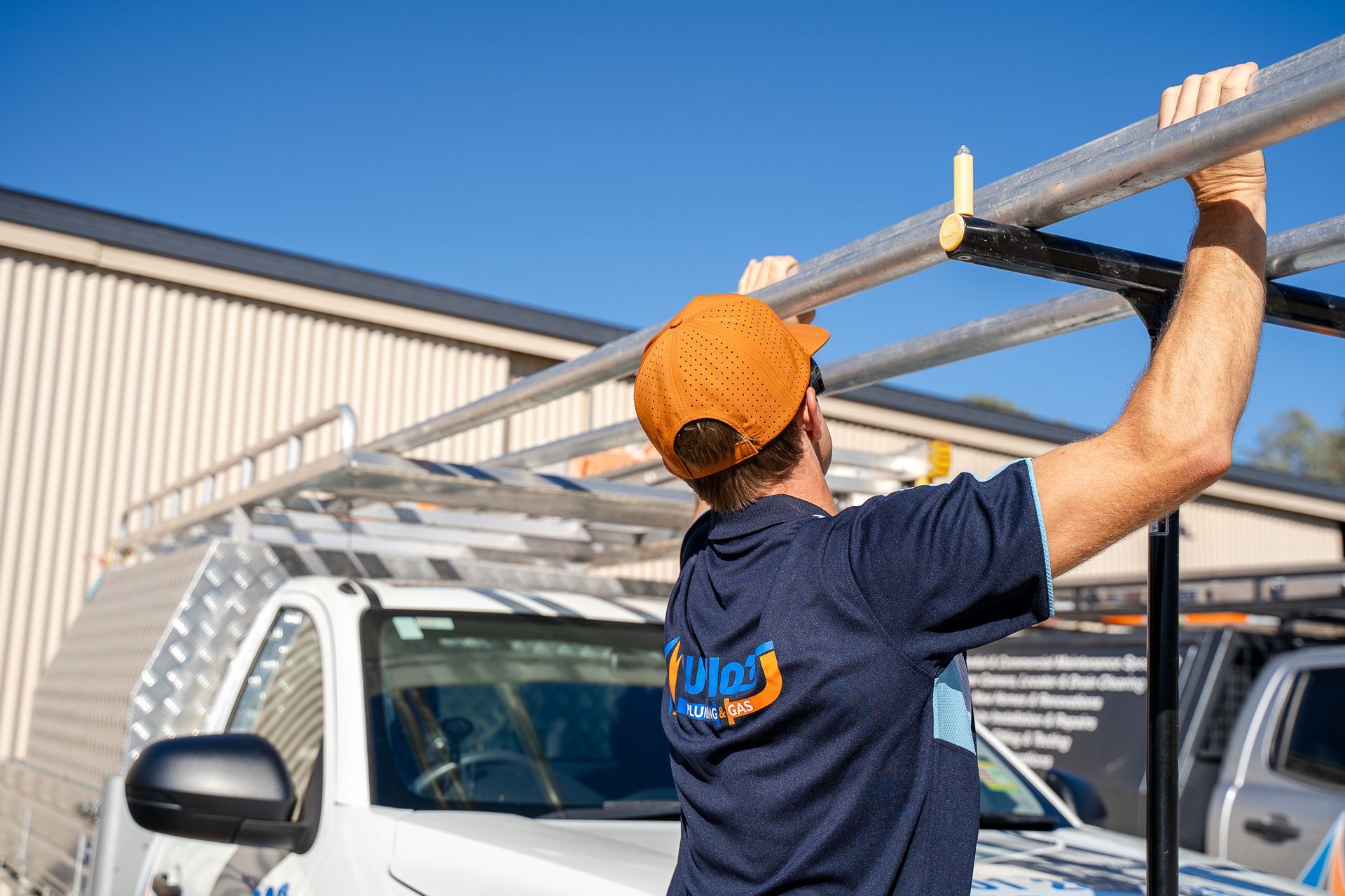 A Man in A Blue Shirt Is Lifing A Steel Rod — Wello's Plumbing & Gas in Thurgoona, NSW
