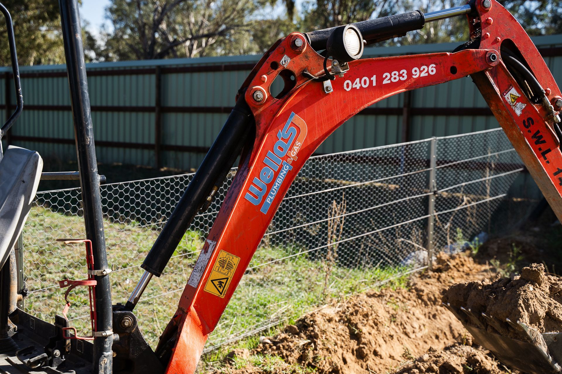 An Excavator Is Digging a Hole in The Dirt in A Field — Wello's Plumbing & Gas in Thurgoona, NSW