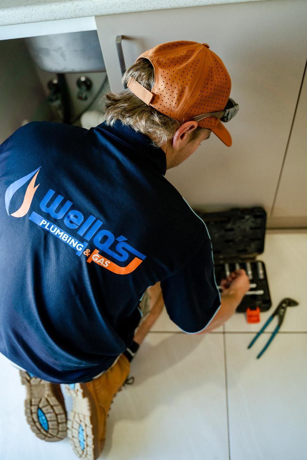 A Man is Working on a Sink in a Kitchen — Wello's Plumbing & Gas In Thurgoona, NSW