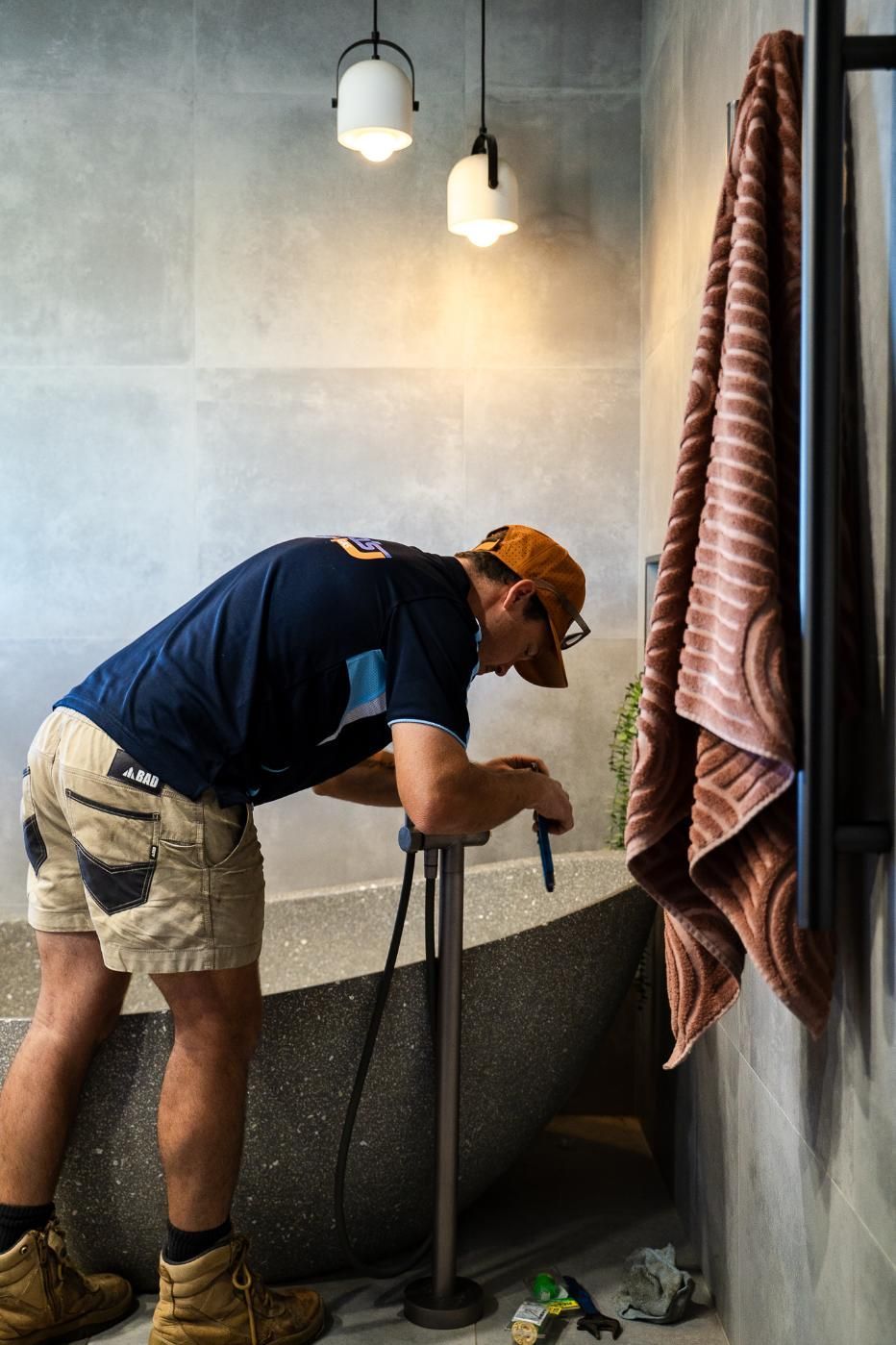 A Man is Working on a Bathtub in a Bathroom — Wello's Plumbing & Gas In Thurgoona, NSW