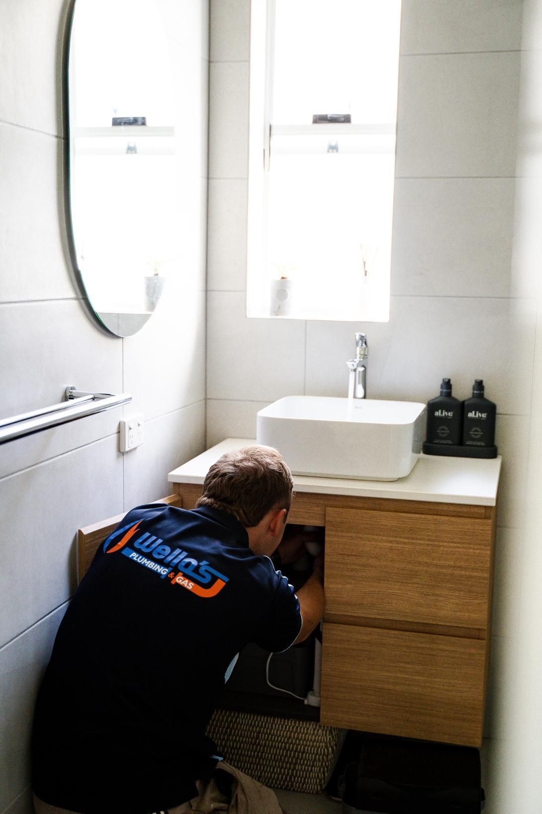 A Man is Fixing a Sink in a Bathroom — Wello's Plumbing & Gas In Thurgoona, NSW