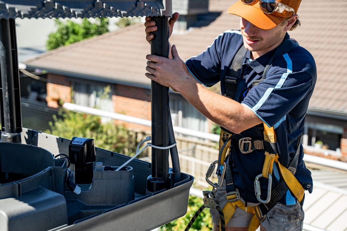 A Man Wearing a Hard Hat and Safety Harness is Working on a Roof — Wello's Plumbing & Gas In Thurgoona, NSW