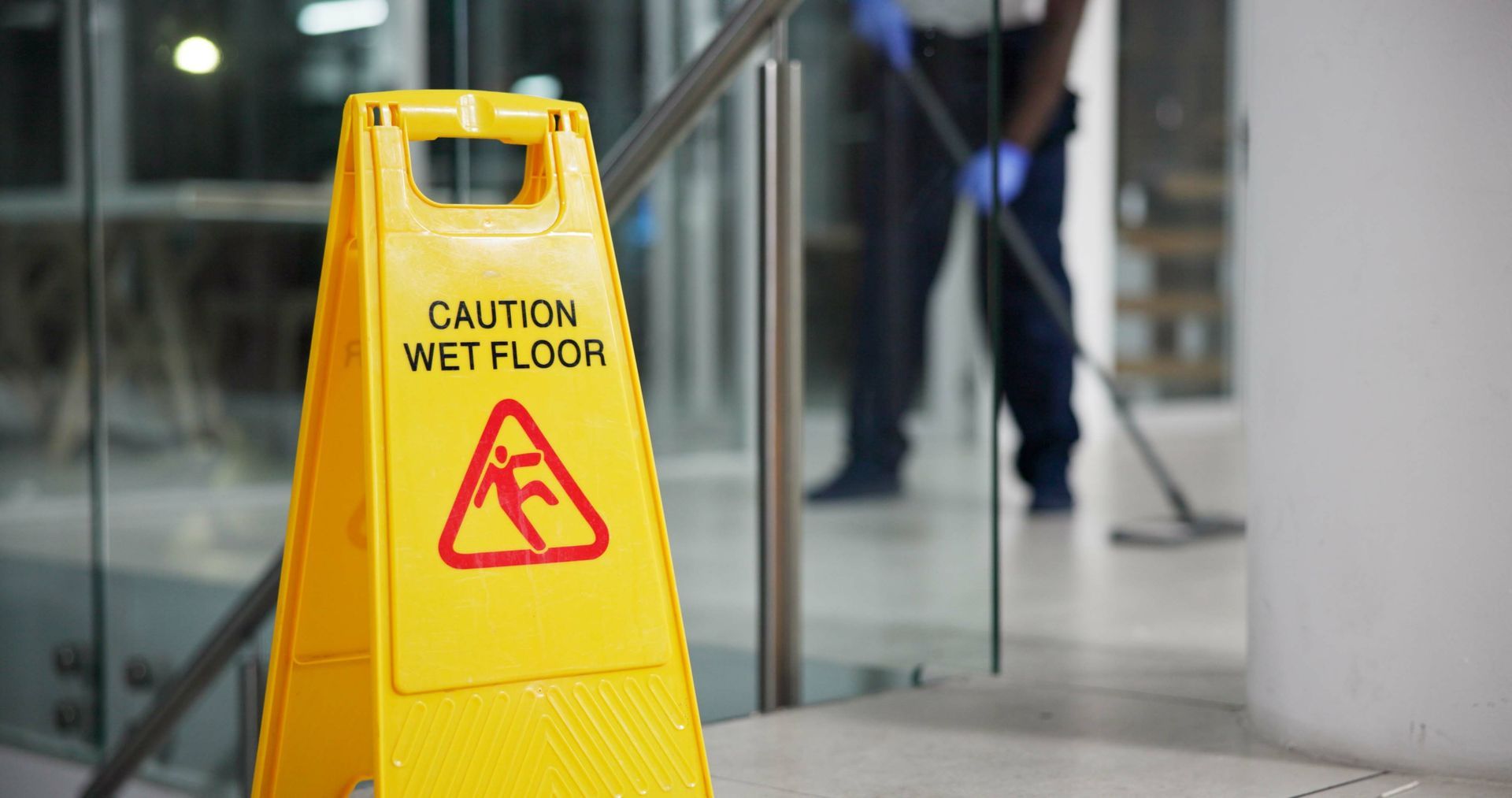 A man is mopping the floor next to a yellow caution wet floor sign.