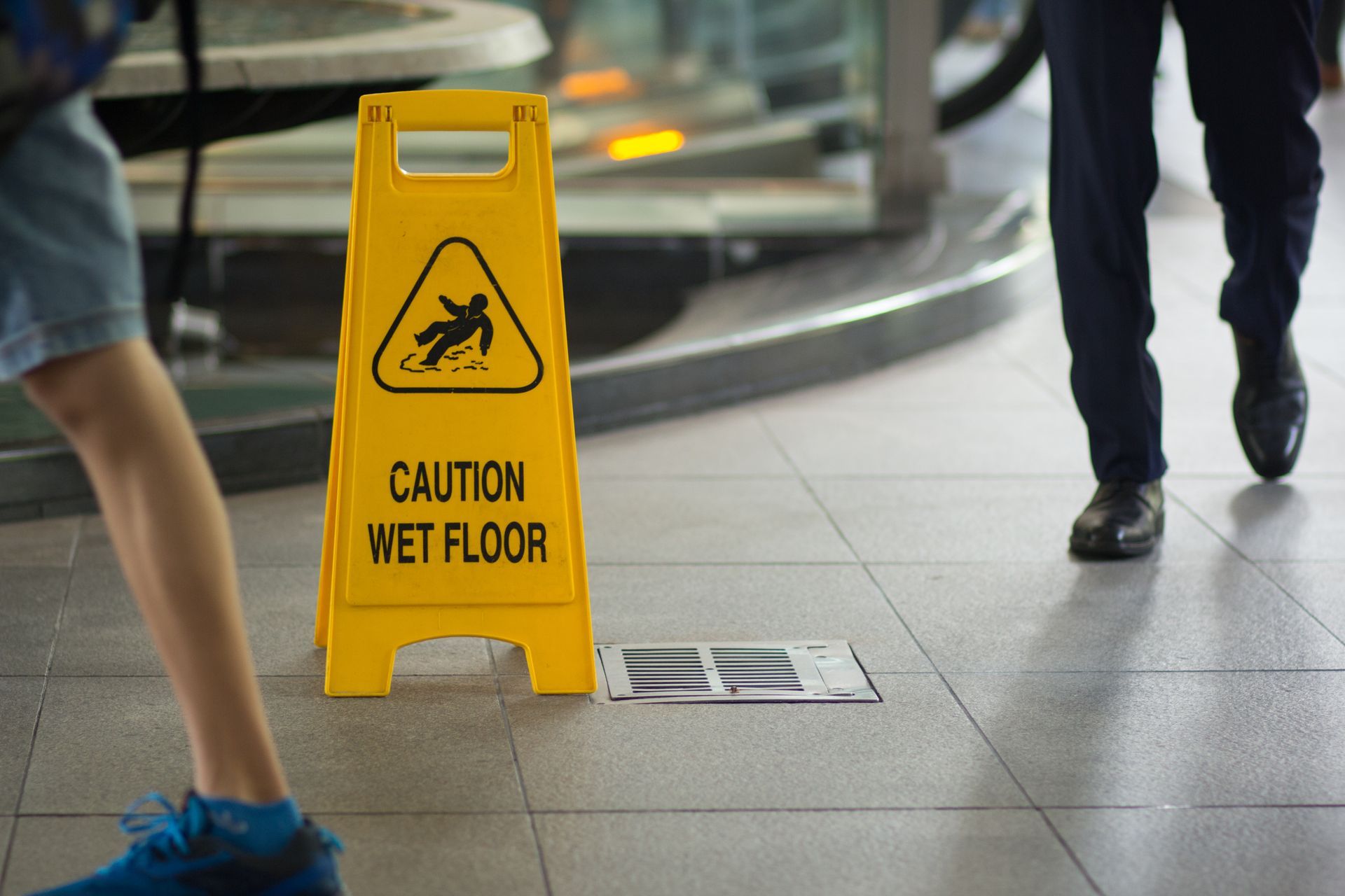 Yellow caution wet floor sign on a tiled floor with pedestrians walking nearby, illustrating a slip 