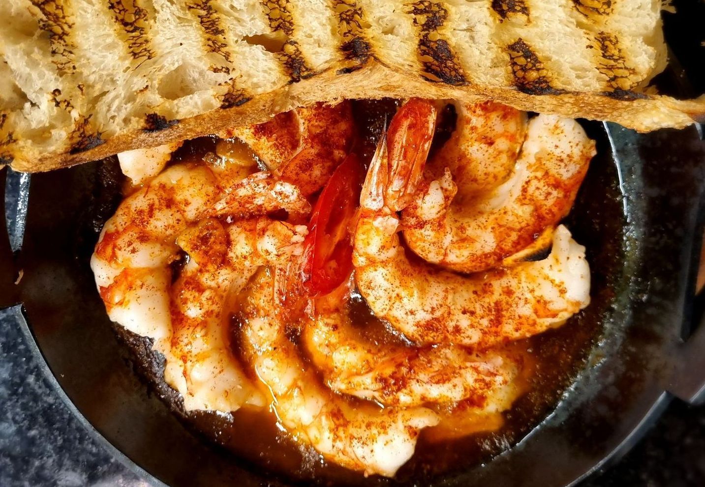 Una sartén llena de camarones y pan sobre una mesa.