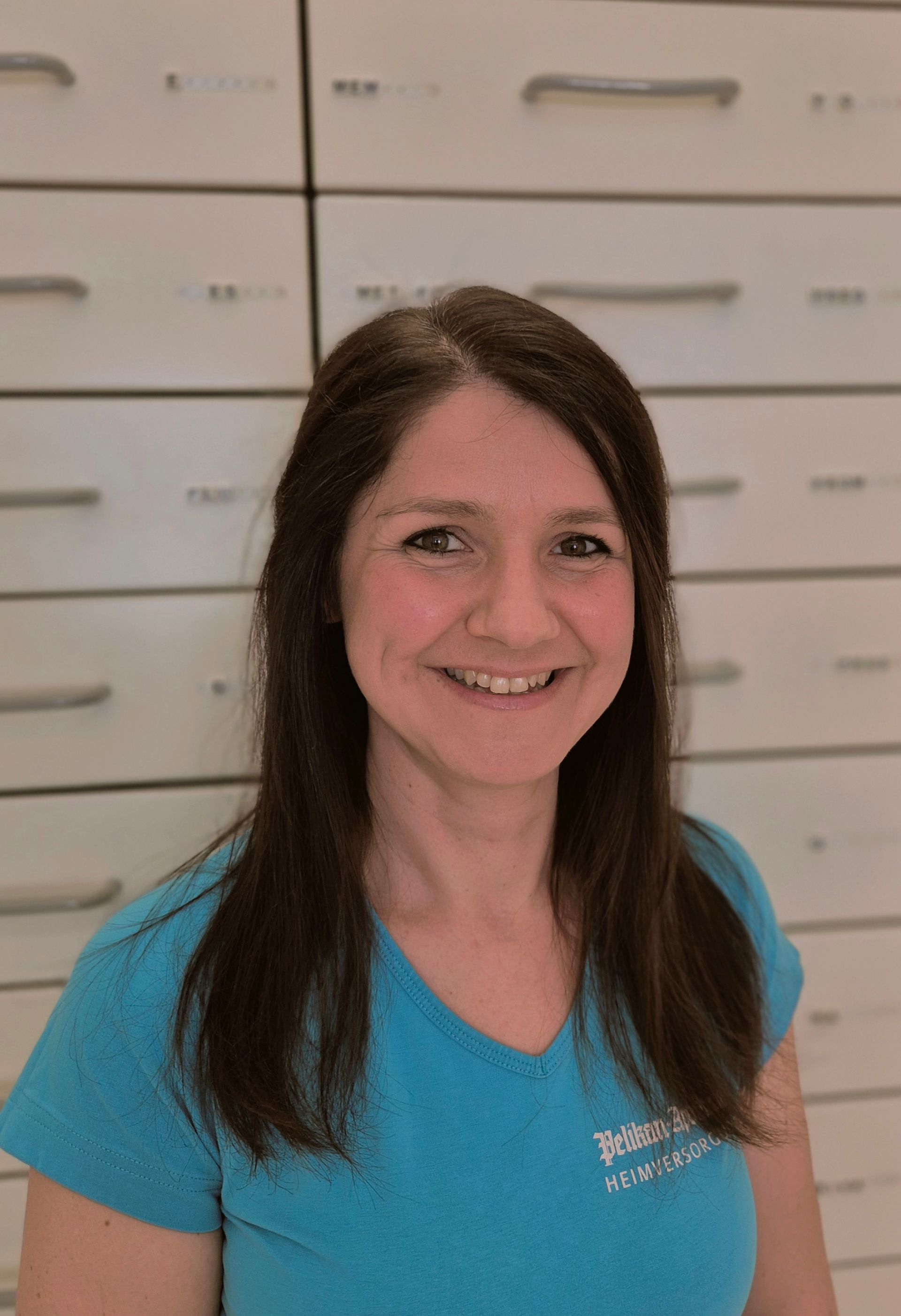 Eine Frau sitzt mit einem Laptop an einem Tisch und schreibt auf einem Blatt Papier.